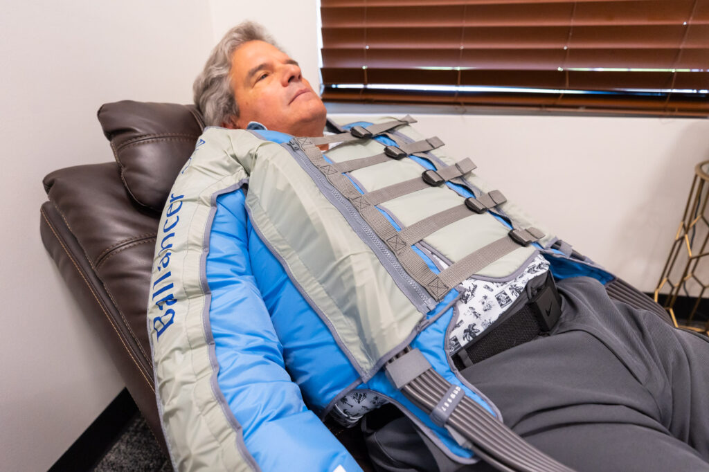 A patient lies down with his eyes closed as he relaxes in the Ballancer Pro suit for lymphatic drainage massage near Prosper, TX.