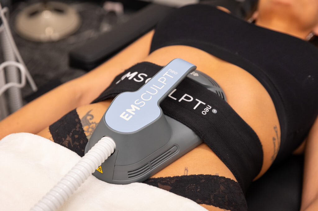 A patient lies down with an Emsculpt NEO device attached to her abdomen as she tries to learn how to lose belly fat in Dallas.